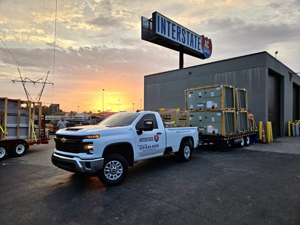 Interstate AC truck transporting new commercial HVAC units on a trailer at sunset in Nashville, TN.