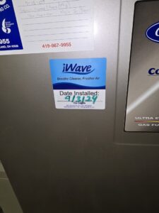 An iWave air purifier installation sticker on an HVAC unit, showing the installation date by Pugh Heating & Air Conditioning in Holland, OH.