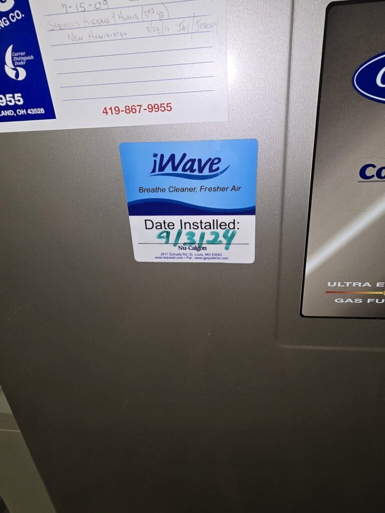 An iWave air purifier installation sticker on an HVAC unit, showing the installation date by Pugh Heating & Air Conditioning in Holland, OH.