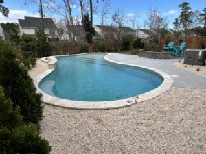 A beautiful kidney-shaped swimming pool with surrounding gravel landscaping and a fire pit, installed by Salty Reef Pools LLC in Summerville, SC.