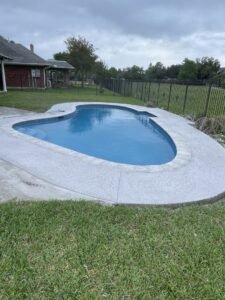 A newly renovated kidney-shaped swimming pool with clean water and fresh concrete decking by I10 Pool Plastering LLC in Kenner, LA.
