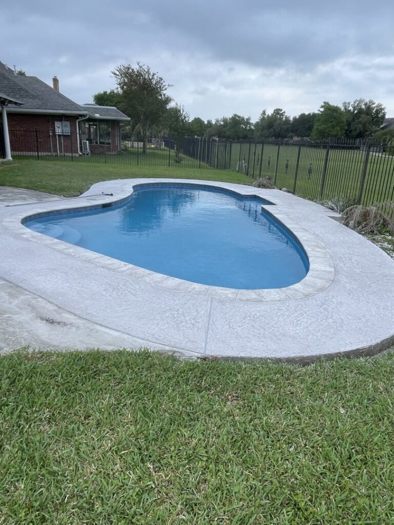 A newly renovated kidney-shaped swimming pool with clean water and fresh concrete decking by I10 Pool Plastering LLC in Kenner, LA.
