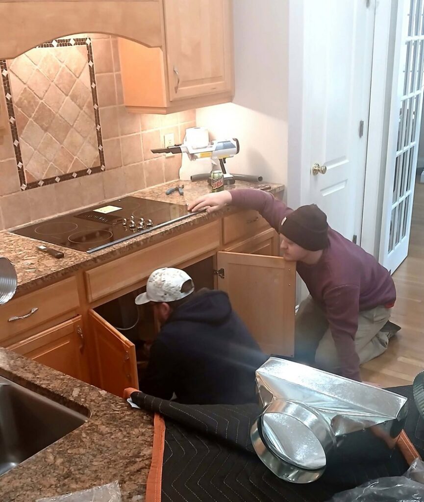 Electricians installing a kitchen cooktop and range hood ventilation at a home by True Vine Electric in Raleigh, NC