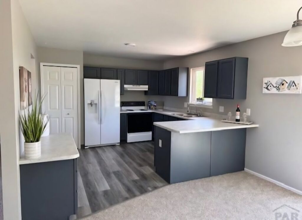 A kitchen with new grey plank flooring and carpet in the dining area by Carpet Clearance Warehouse Pueblo, CO.