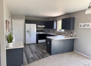A kitchen with new grey plank flooring and carpet in the dining area by Carpet Clearance Warehouse Pueblo, CO.