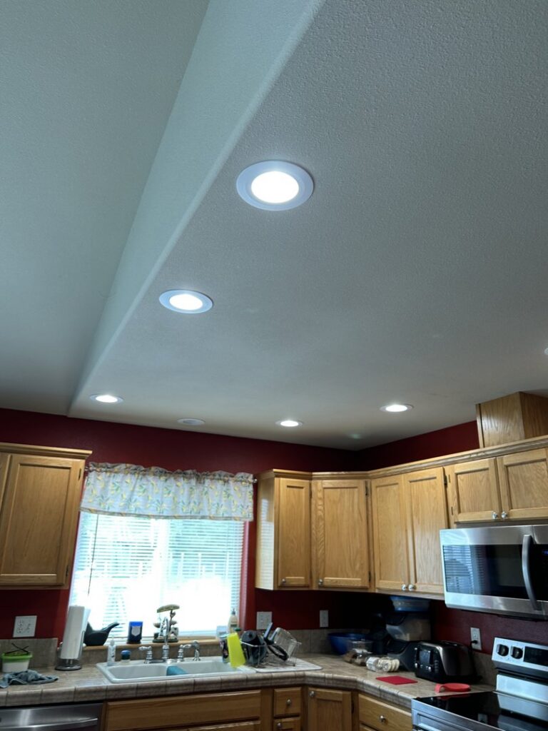 A modern kitchen featuring newly installed recessed lighting in the ceiling, a completed electrical project by Devaney Electric Co. in Lacey, WA.