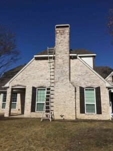 A ladder leaning against a tall brick chimney on a house, indicating chimney service by HBR Hearth and Chimney in Dallas, TX