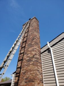 A tall ladder leaning against a brick chimney, ready for service by Clean Sweep Chimney Service in Saint Charles, MO.