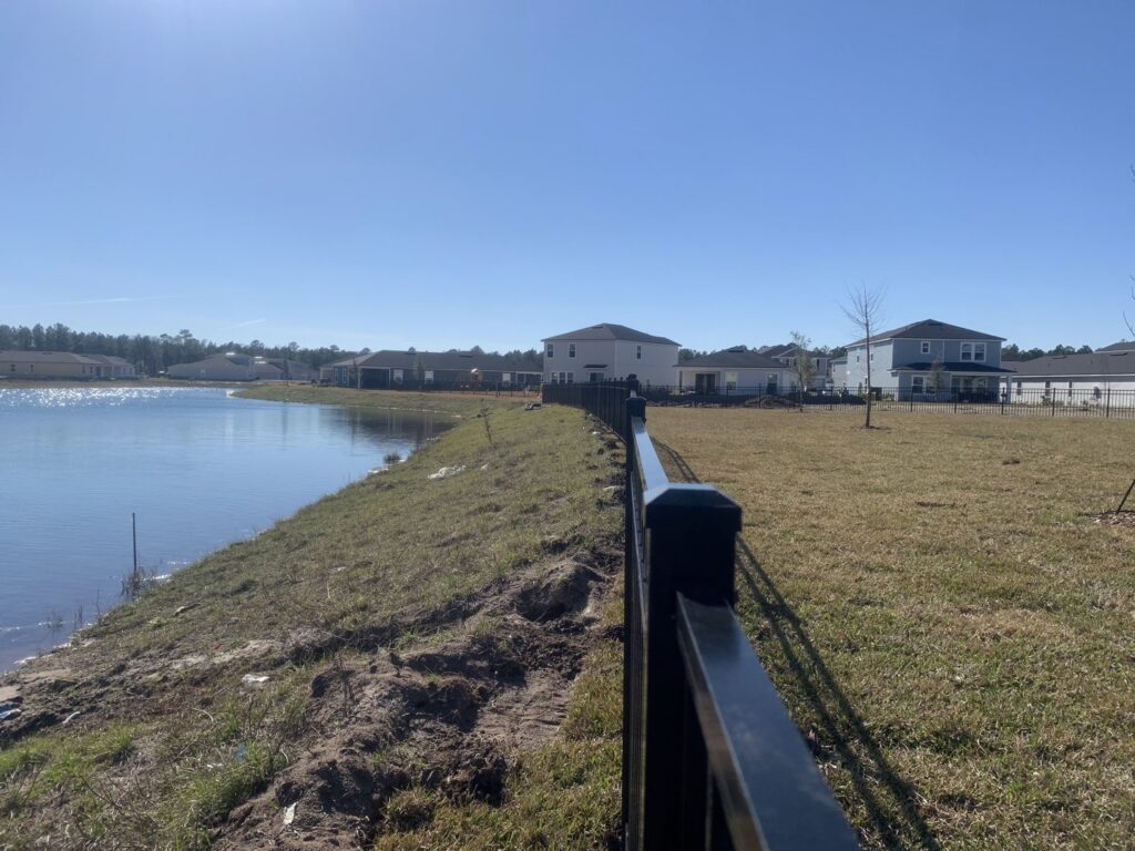 A newly installed black aluminum fence running along a lakefront property by Top Fence LLC in Jacksonville, FL.