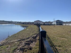 A newly installed black aluminum fence running along a lakefront property by Top Fence LLC in Jacksonville, FL.