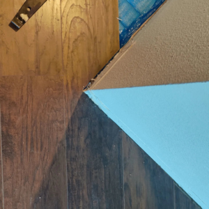 Close-up of laminate flooring planks and blue underlayment installed near a wall by Steam Vs. Soil Carpet Cleaning in San Diego, CA