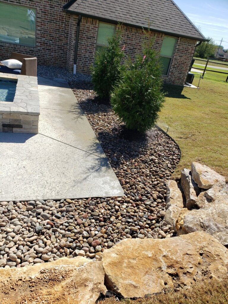 A beautifully landscaped area with decorative rocks, small trees, and a concrete path by GAMAS Lawn Care Services in Tulsa, OK.
