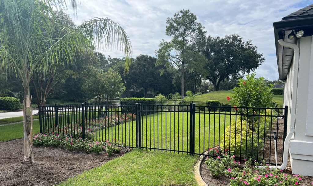 A beautifully landscaped backyard enclosed by a black aluminum fence, expertly installed by Exacta FENCE LLC in Jacksonville, FL.