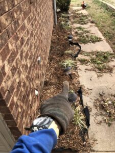 A gloved hand pointing at a freshly mulched landscape bed with new plants and solar lights by A & A Lawn Care Service LLC in Edmond, OK.