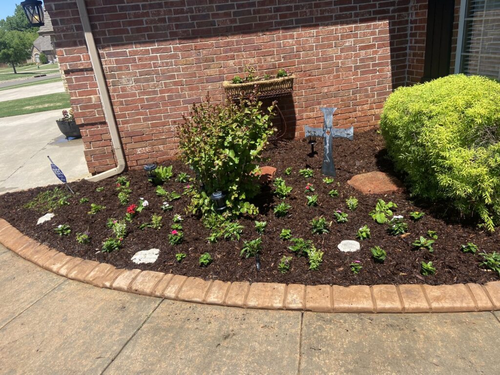 A beautifully landscaped flower bed with fresh mulch, various plants, and decorative elements, completed by Perez Lawn Care llc in Oklahoma City, OK.