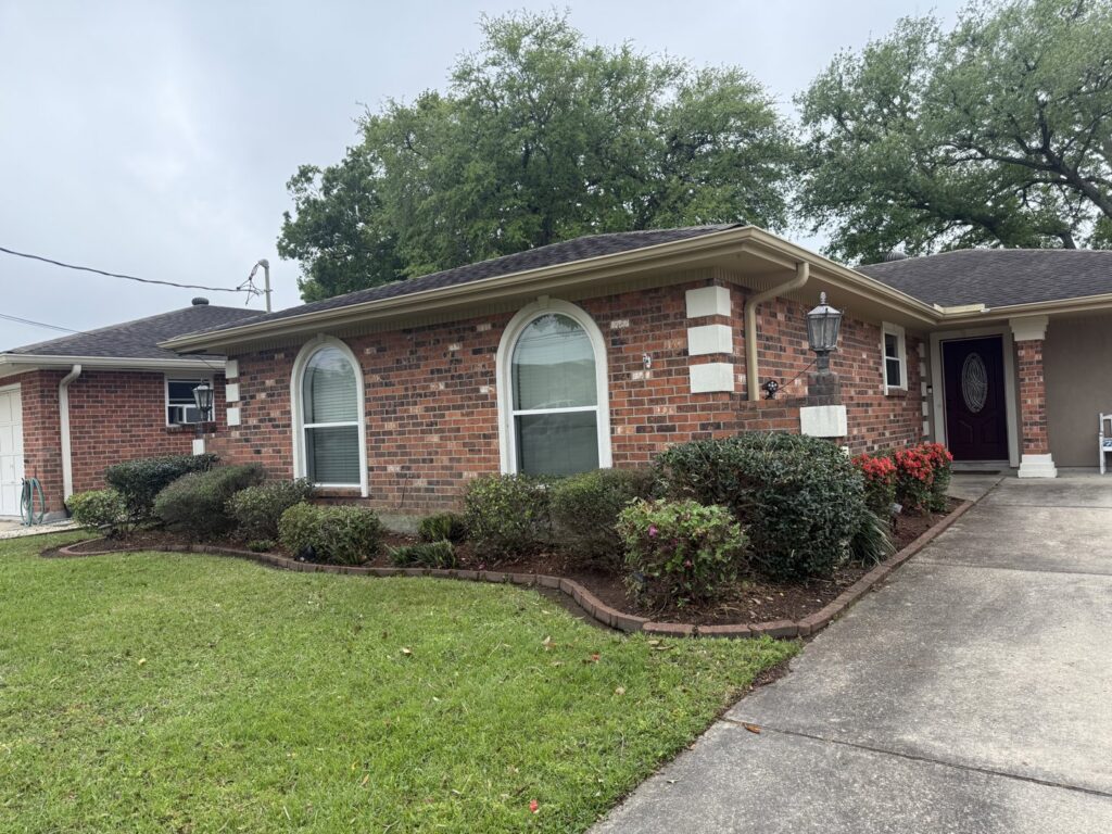 A beautifully landscaped front garden with various bushes and fresh mulch around a brick house by God's Sight Lawn & Gardens LLC in New Orleans, LA