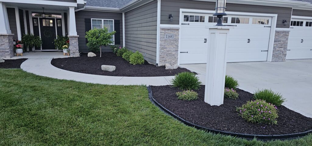 A well-maintained landscape bed with dark mulch and a concrete walkway by ALL Lawn Care Service in Saint Louis, MO