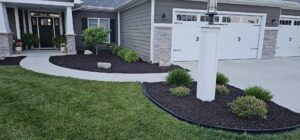A well-maintained landscape bed with dark mulch and a concrete walkway by ALL Lawn Care Service in Saint Louis, MO