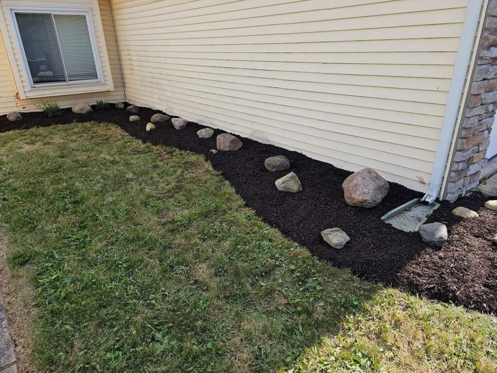 A neatly landscaped bed with dark mulch and decorative rocks by ALL Lawn Care Service in Saint Louis, MO