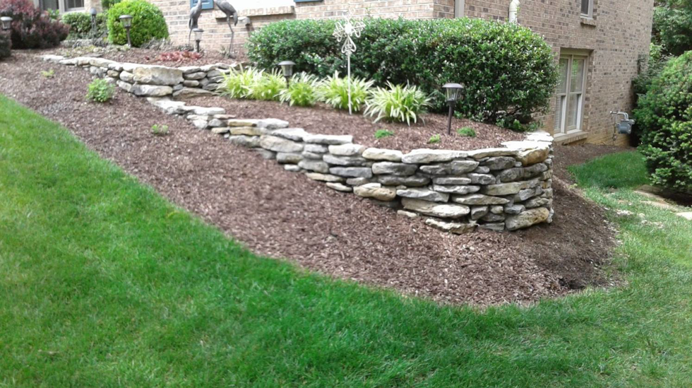 A beautifully landscaped yard with a stone retaining wall and fresh mulch, maintained by Tim's Lawn Care Service Inc in Lafayette, LA.