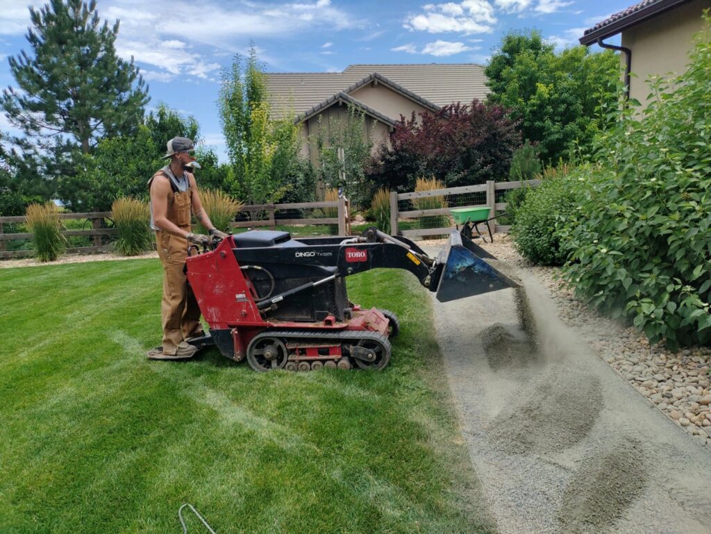 A landscaper using a Toro Dingo compact utility loader to spread gravel for a path, a service by Front Range Finest in Fort Collins, CO.
