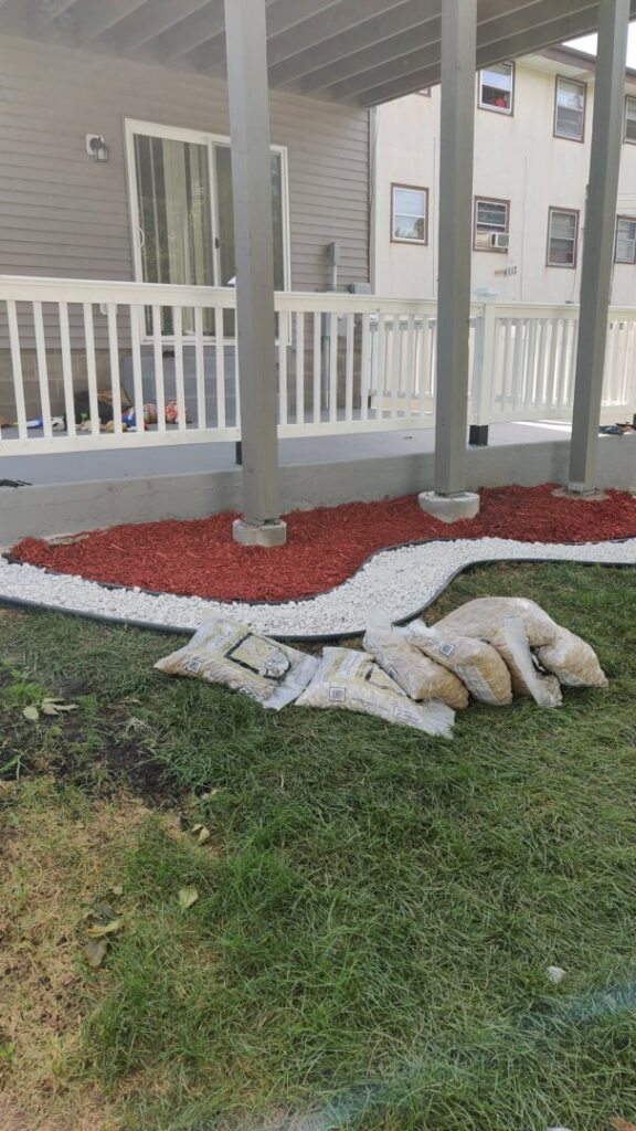 Landscaping under a deck featuring red mulch and white decorative stones, a service by K&R Lawn Care in Pass Christian, MS.