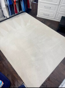 A large, light-colored area rug on a dark wood floor, freshly cleaned with visible cleaning lines by Ype Cleaning LLC in Monroe, NC.