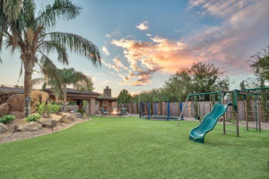 A spacious backyard with artificial turf and a children's play area installed by Jabara's Turf Outlet in Wichita, KS.