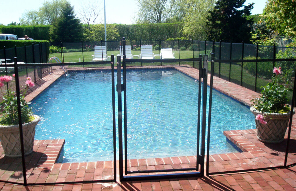 A spacious backyard featuring a pool enclosed by a black mesh safety fence, installed by Pool Guard in North Charleston, SC.