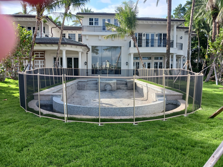 A large backyard pool secured with a light-colored mesh safety fence by All Brand Pool Fence in Fort Lauderdale, FL.