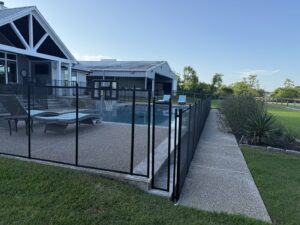 A large backyard swimming pool secured with a black mesh safety fence by Lone Star Pool Fence in Houston, TX.