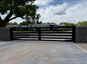 A large black horizontal slat gate with gabion stone pillars, installed by City Iron LLC in Albuquerque, NM.