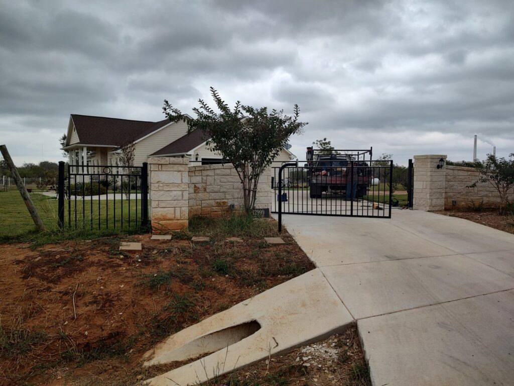 A large black metal fence and gate with stone pillars at a residential driveway entrance by Serrato's Fence & Welding in San Antonio, TX.