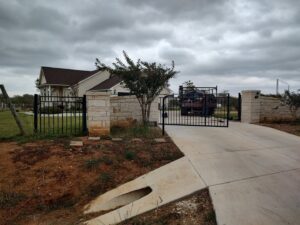 A large black metal fence and gate with stone pillars at a residential driveway entrance by Serrato's Fence & Welding in San Antonio, TX.