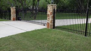 A large black metal driveway gate with elegant stone pillars installed by Serrato's Fence & Welding in San Antonio, TX.