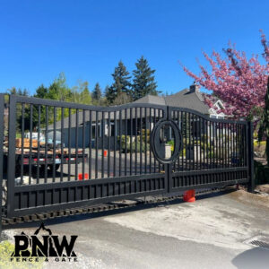 A large black ornate metal driveway gate with a decorative circular emblem, expertly installed by PNW FENCE in Lewiston, ID.