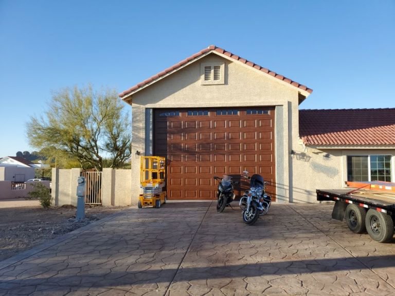 A large brown garage door installed on a residential property, with a scissor lift nearby, by Iconic Garage Door Service in Queen Creek, AZ.