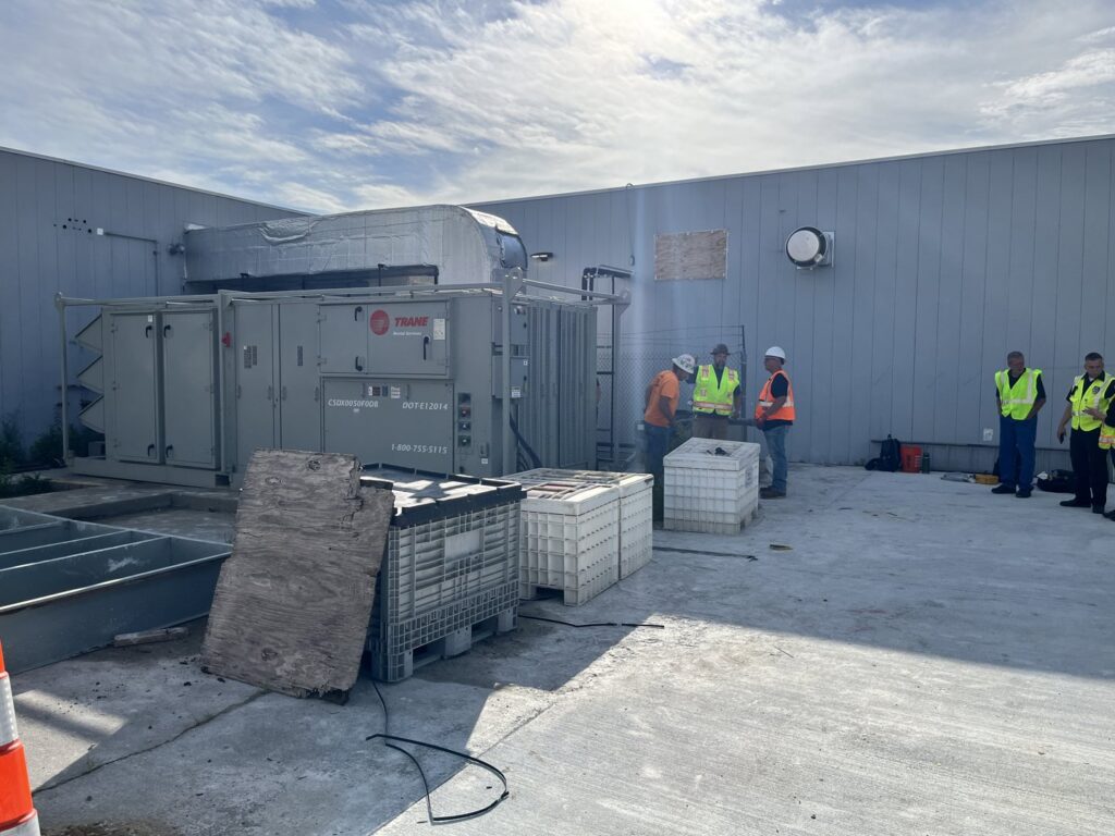 Workers from DMC Service, Inc. installing or servicing a large commercial Trane HVAC system next to a building in Olathe, KS.