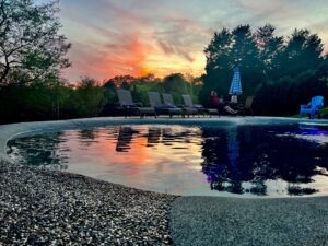 A large dark-bottom pool reflecting a beautiful sunset, a completed installation by The Staycation Builders in Fort Wayne, IN.