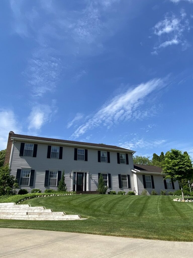 A large residential house with a meticulously striped lawn, showcasing the expert mowing services of Roots Lawn Care Solutions in Granger, IN.