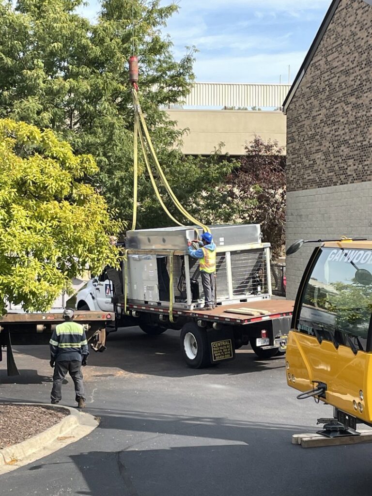 Workers overseeing the installation of a large commercial HVAC unit with a crane for Nortek Environmental, Inc. in Naperville, IL.