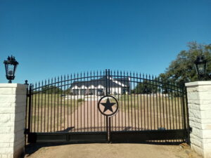 A grand black iron entrance gate with a Texas star emblem, flanked by stone pillars and lanterns, by Superior Fence Co. of San Antonio, TX.