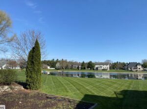 A large residential lawn with distinct mowing stripes next to a scenic pond, maintained by Roots Lawn Care Solutions in Granger, IN.