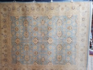 A large light blue and beige patterned rug hanging for display at Khazai Rugs in Lexington, KY