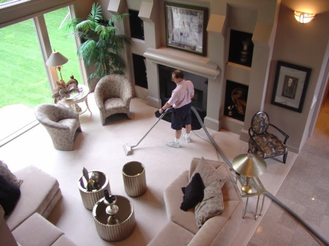 A technician cleaning a large carpeted living room with a professional carpet cleaning wand at Referral Cleaning and Restoration Inc. in Fort Wayne, IN.