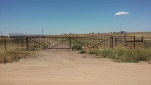 A large metal driveway gate installed across a dirt road leading to a field by Done Wright Fencing and Welding in Denver, CO.