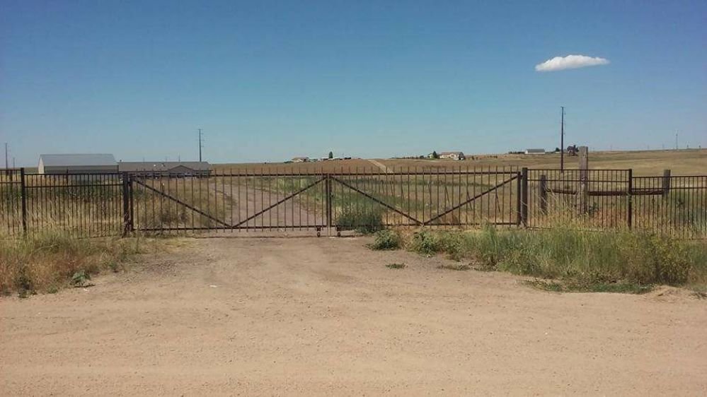A large metal driveway gate installed across a dirt road leading to a field by Done Wright Fencing and Welding in Denver, CO.