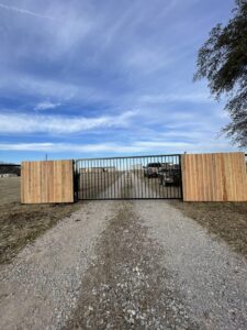 A large metal driveway gate flanked by wooden fence sections installed by Backyard Builders in Rockford, MI.
