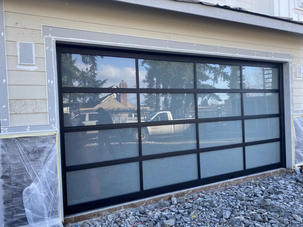 A large modern black framed glass garage door installed on a house under construction by Independent Garage Doors LLC in Tacoma, WA.