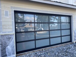 A large modern black framed glass garage door installed on a house under construction by Independent Garage Doors LLC in Tacoma, WA.